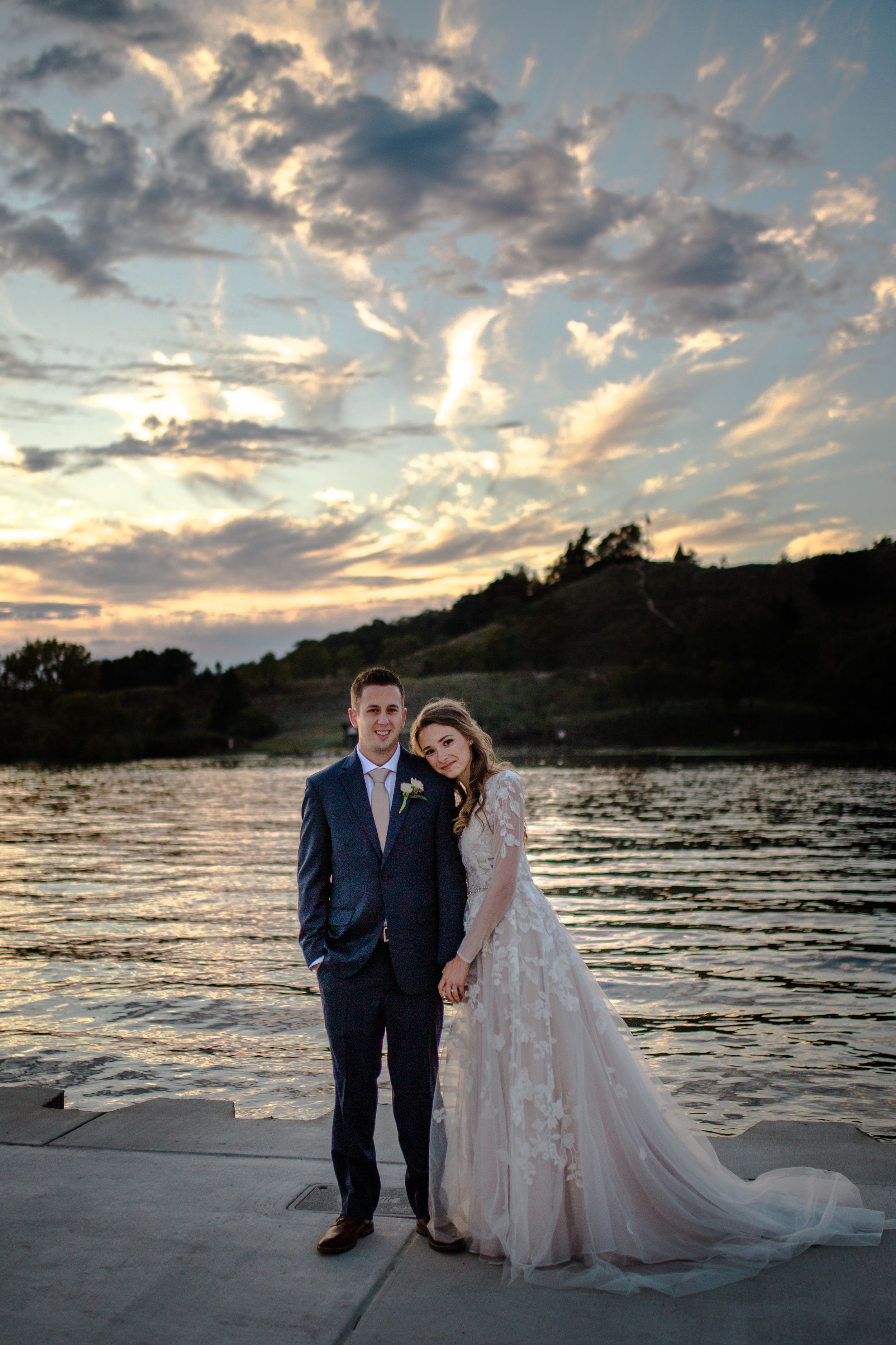 Wedding couple poses on dock at sunset with dramatic cloudy sky.