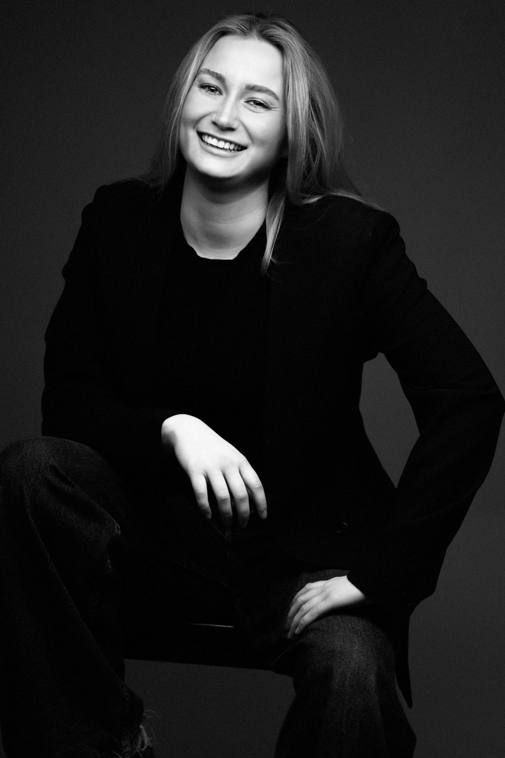 Black and white portrait showing natural joy while seated in casual black attire.