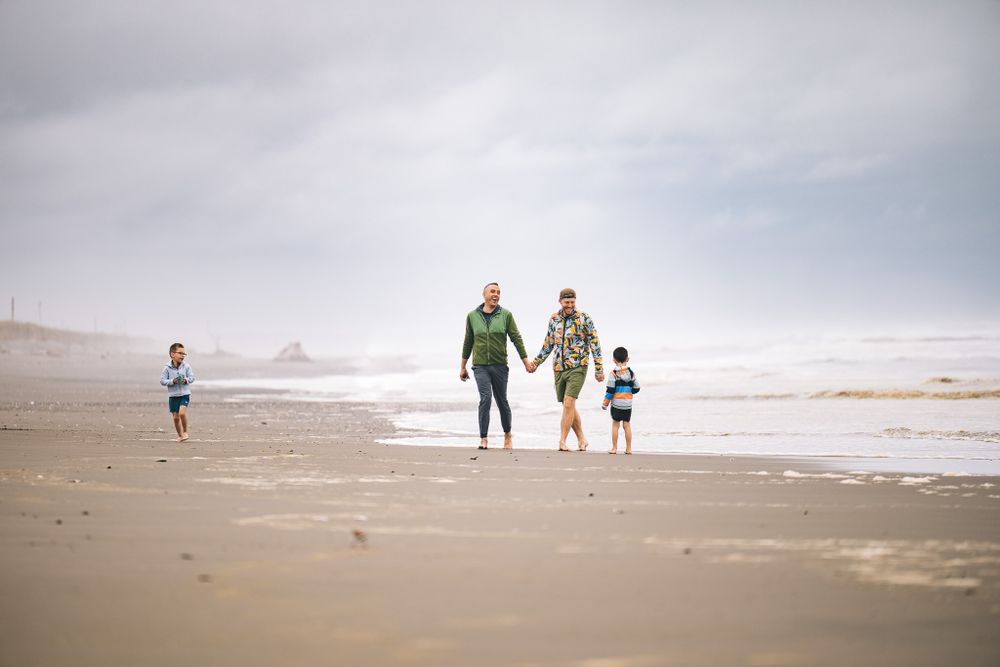 People walking along a foggy beach shoreline with waves and cloudy skies in the distance.