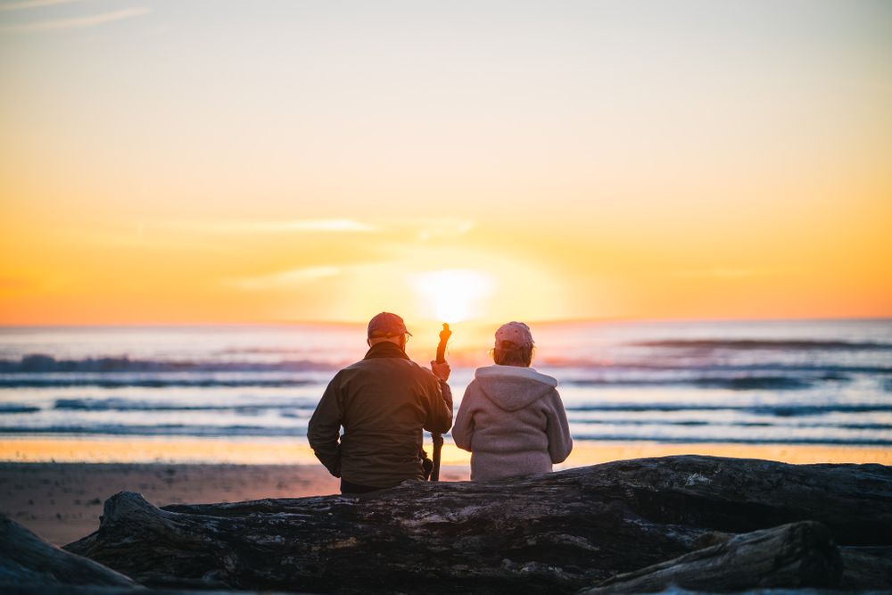 Two people sitting on rocks at the beach watching a golden sunset over the ocean.