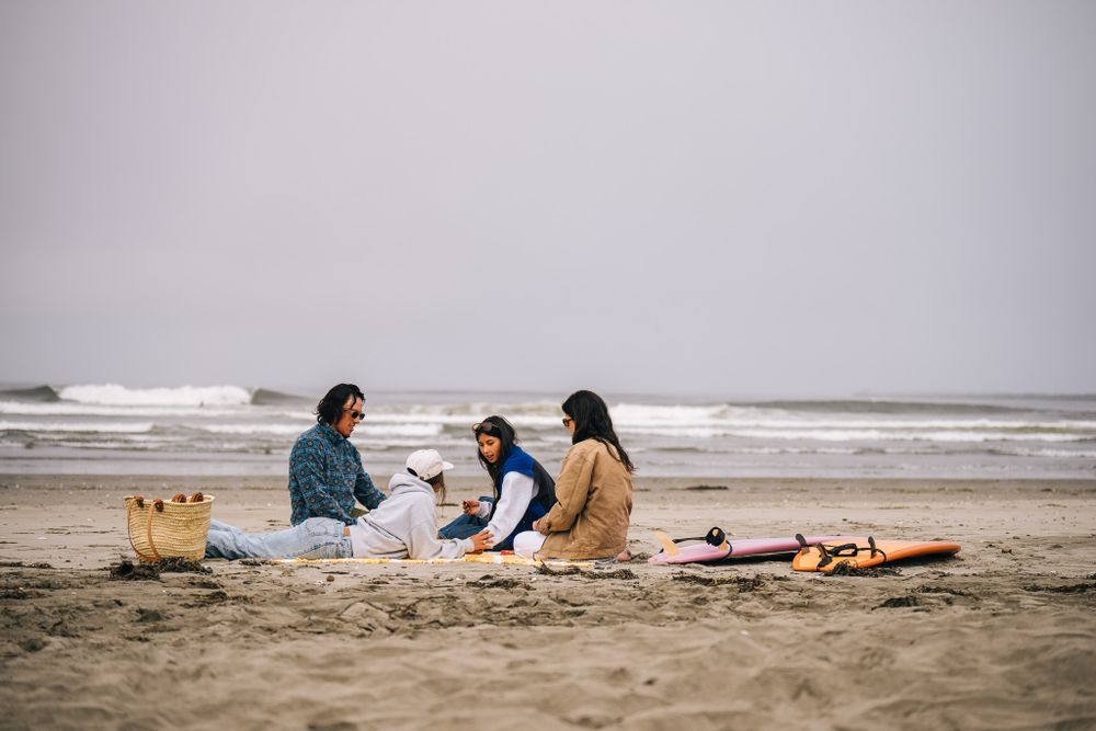 Three people enjoy a peaceful beach picnic on a cloudy day with surfboards laid out beside them.