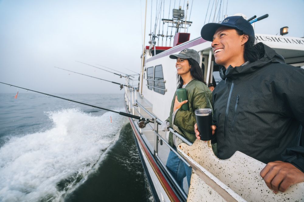 People enjoying a fishing trip aboard a boat as waves splash against the hull on an overcast day at sea.