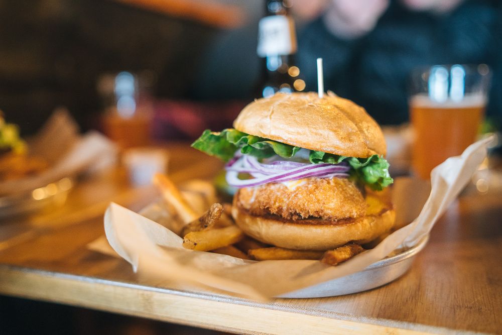 A juicy burger with fresh toppings served on a wooden board with french fries in a casual restaurant setting.