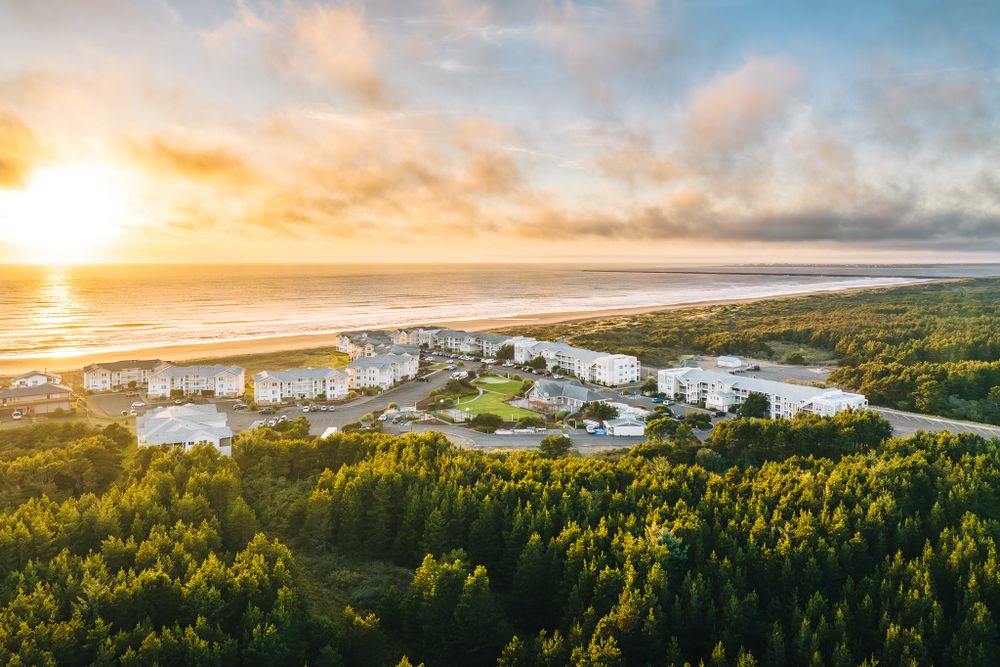Aerial view of coastal resort buildings surrounded by lush forest during golden sunset over ocean.