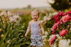 Toddler in floral shorts exploring garden with blooming pink and yellow flowers.