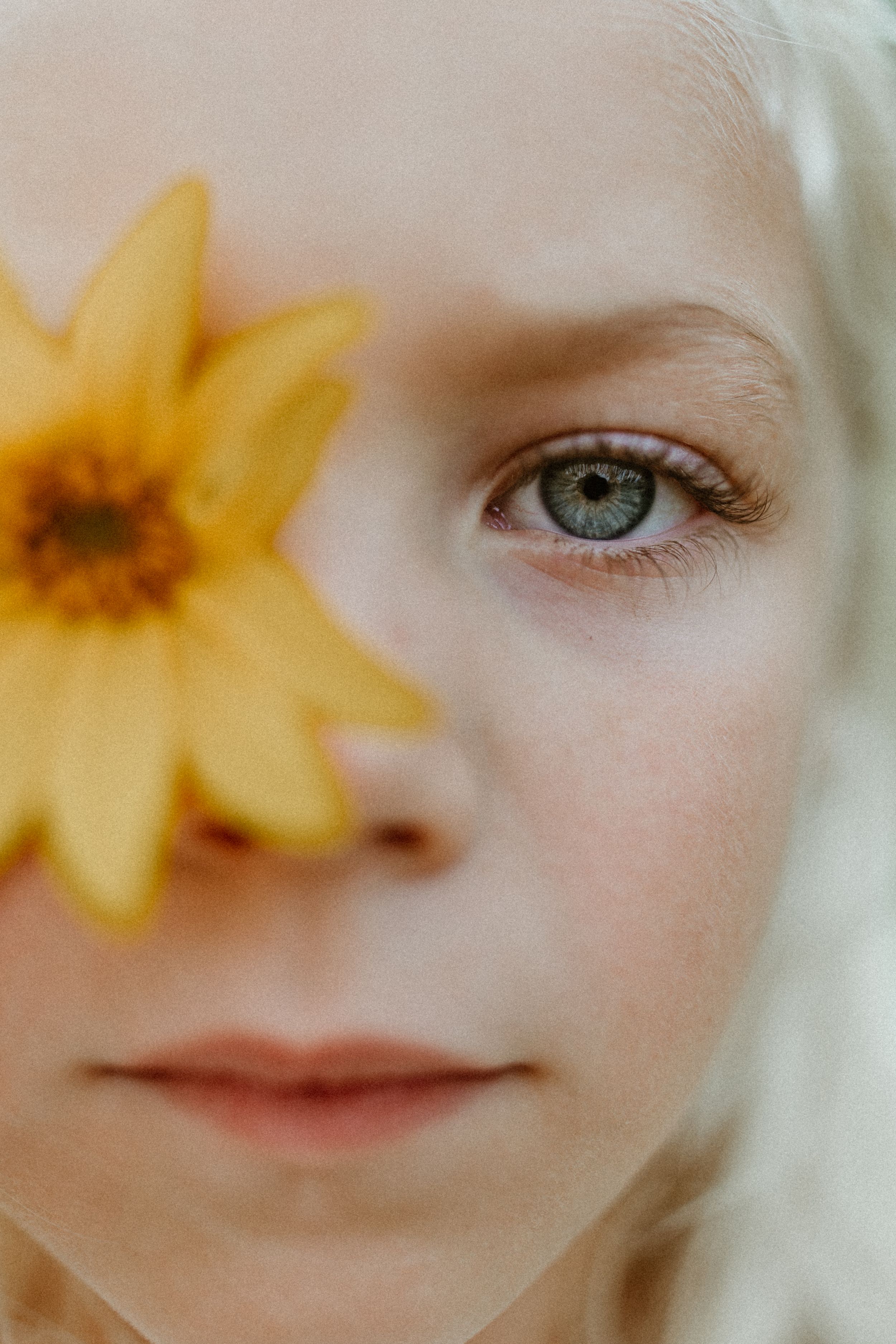 Artistic close-up portrait with a yellow sunflower petal covering half the frame.