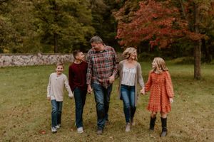 Family of five walking together and smiling on autumn day with colorful trees in background.