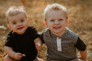 Two young children smiling brightly in an autumn setting with warm golden lighting.