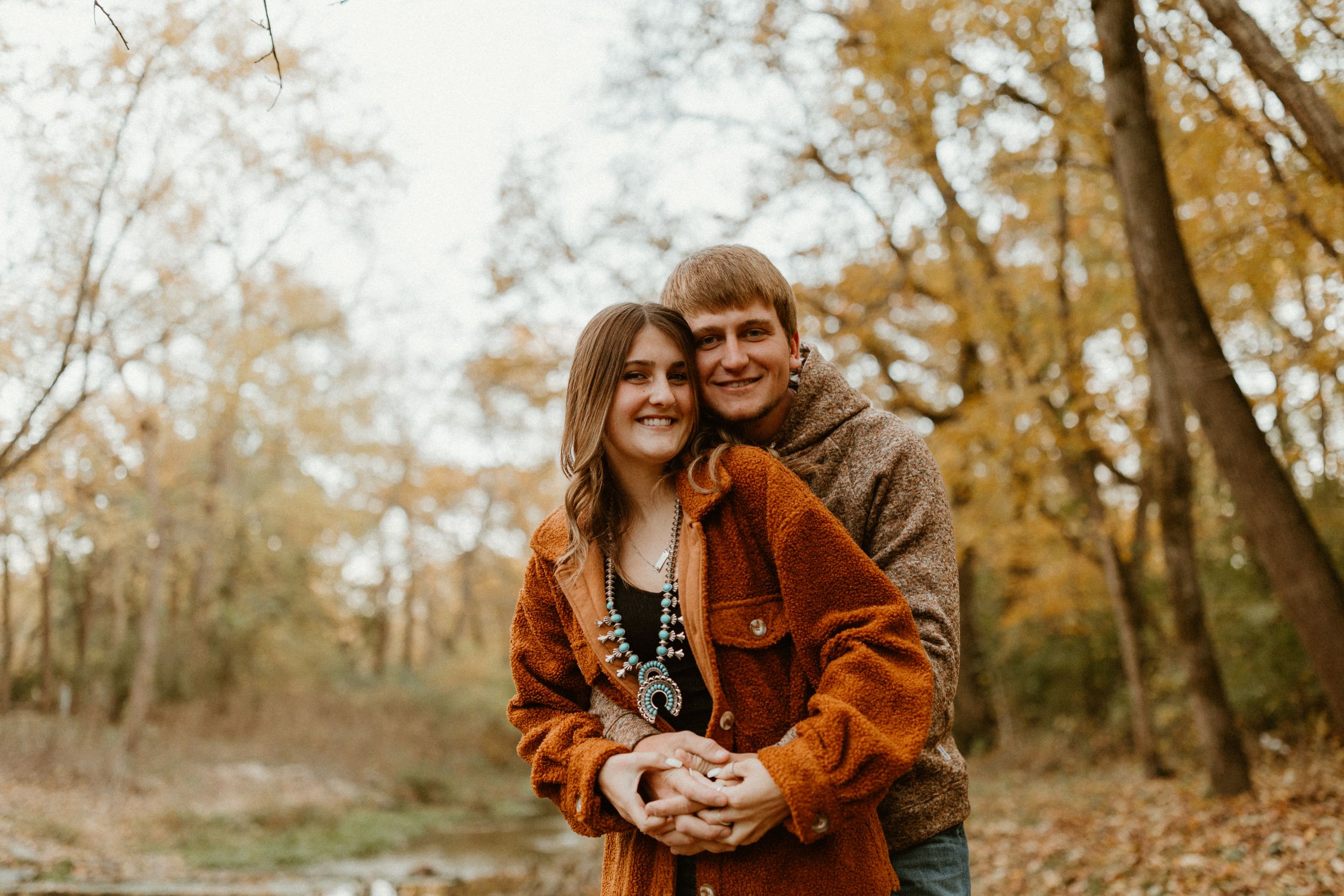 A romantic autumn portrait of a couple embracing outdoors among fall foliage.