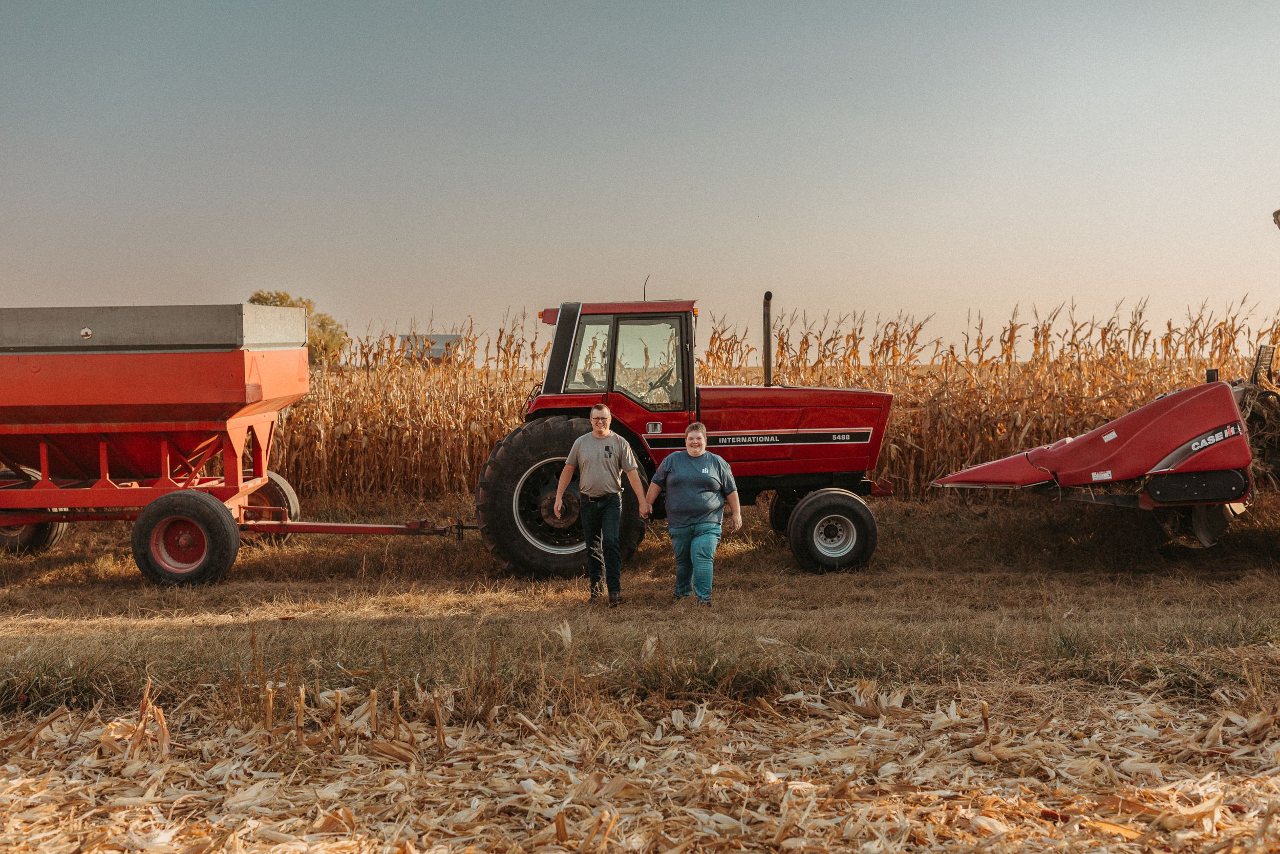 Red tractor and farm equipment lined up in cornfield during harvest season.