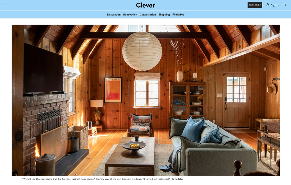 Cozy rustic cabin interior with wood paneling, stone fireplace, plush sofa and hanging paper lantern light fixture.