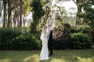 Bride and groom share a kiss under a veil in a lush garden setting on their wedding day.
