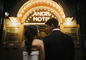 Bride and groom share a romantic moment outside the illuminated Angel Hotel at night.