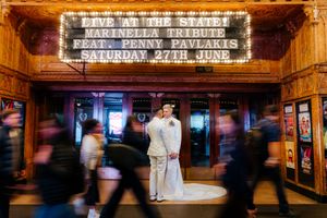 Wedding couple posing outside a theater marquee sign on a busy city street at night.