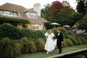 Bride and groom walk hand in hand through lush garden grounds of an elegant estate venue.