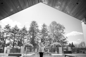 Black and white photo of a bride standing alone under a modern architectural canopy outdoors.