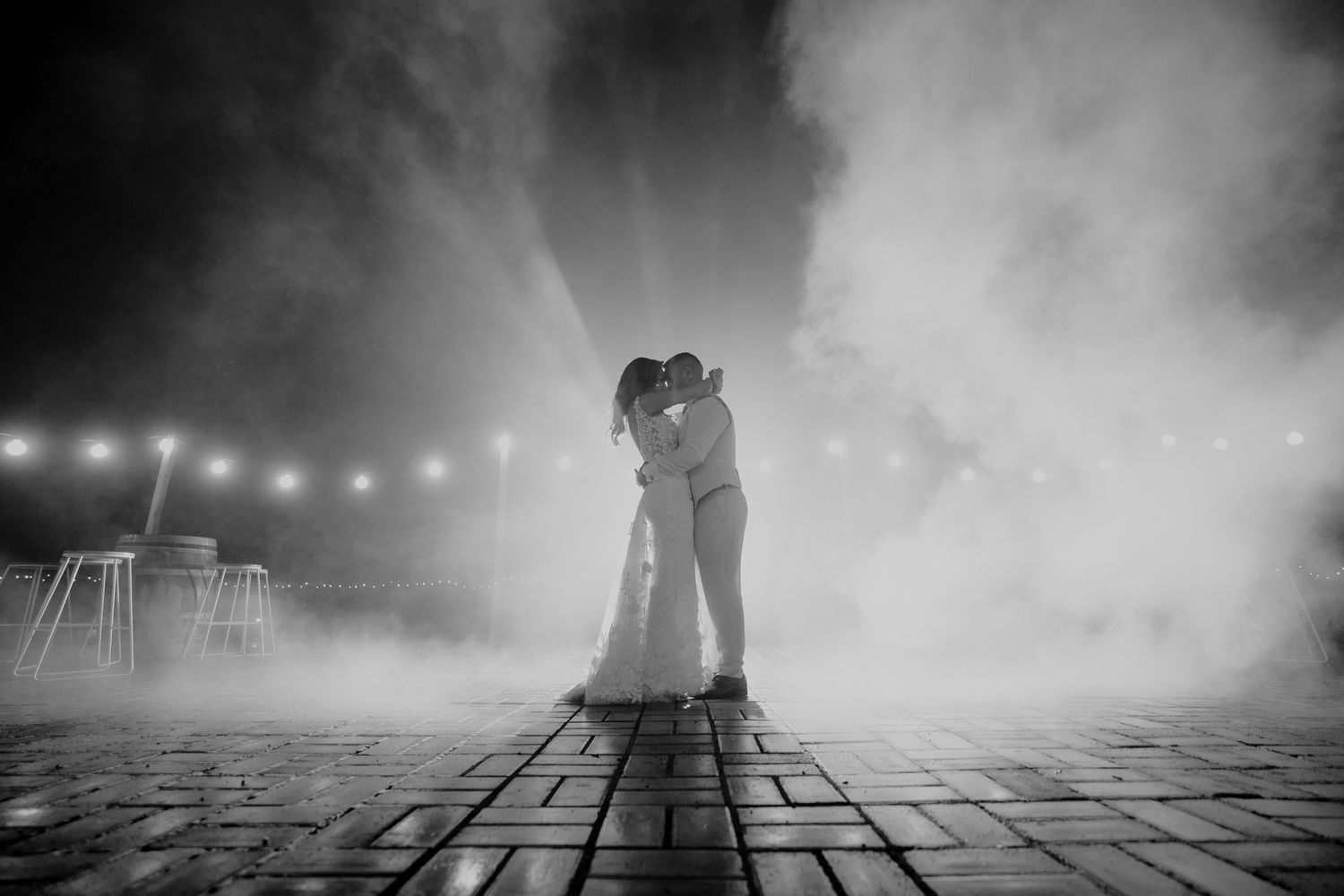Black and white photo of bride and groom sharing first dance surrounded by dramatic fog and lights.