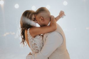 Bride and groom share a passionate kiss during their first dance surrounded by soft white light.
