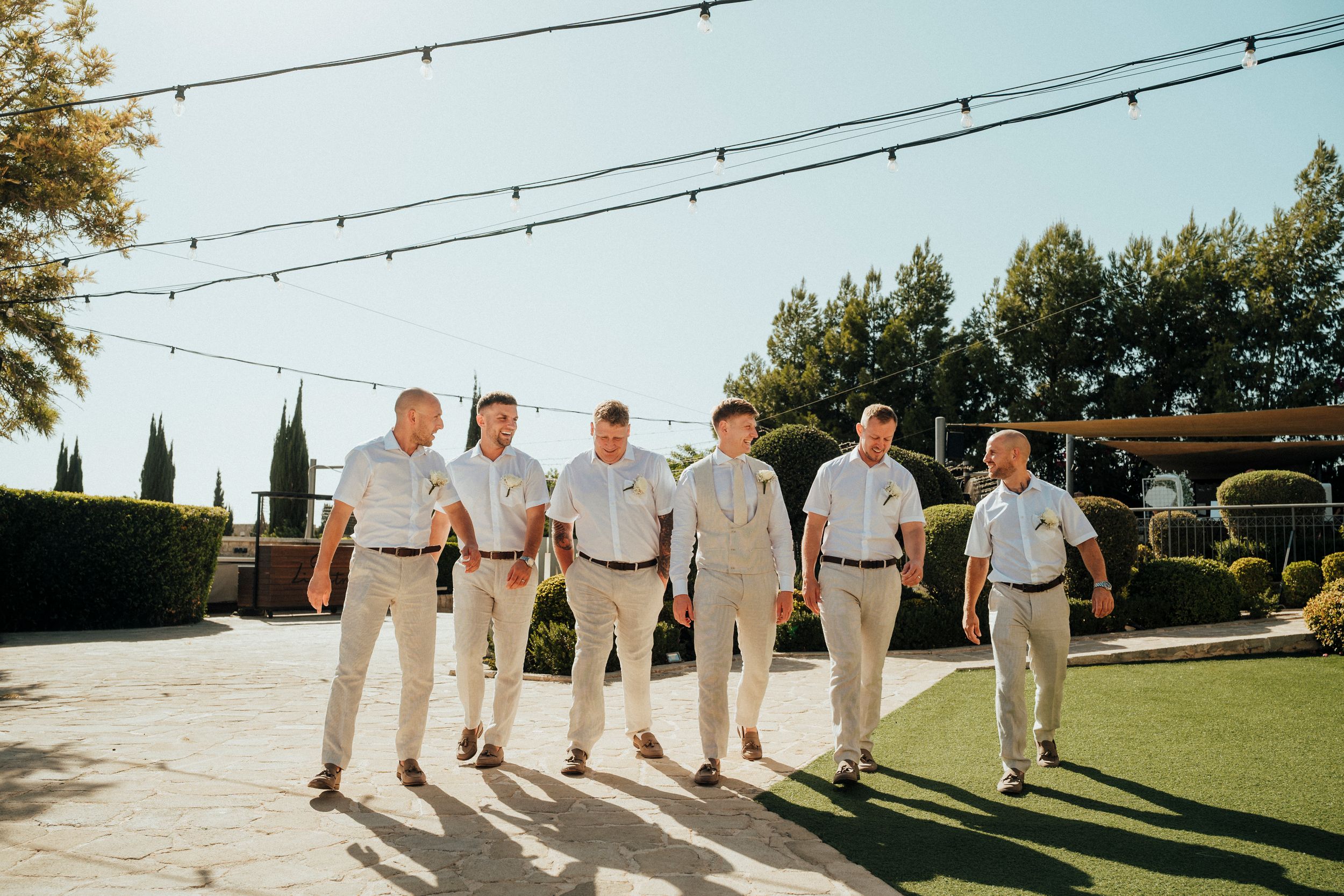 Wedding party members walk together on a grassy lawn during a sunny outdoor celebration.