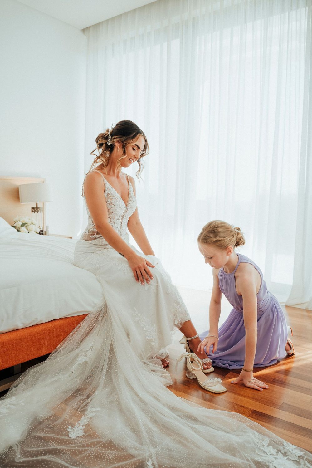 A wedding dress being adjusted and fitted as the bride gets ready with help from an attendant in a purple dress.