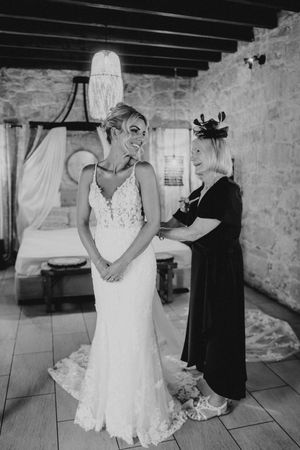 Black and white photos show intimate moments of wedding dress preparations in a rustic stone-walled venue.