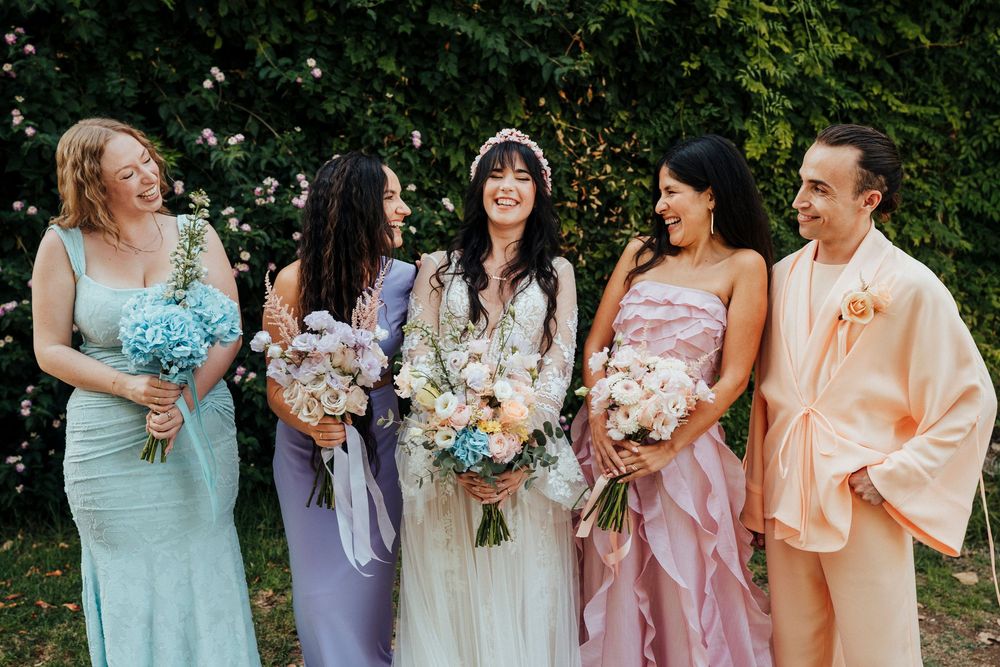 Bridesmaids in pastel dresses of mint, lavender, and blush pink hold bouquets while standing together outdoors.
