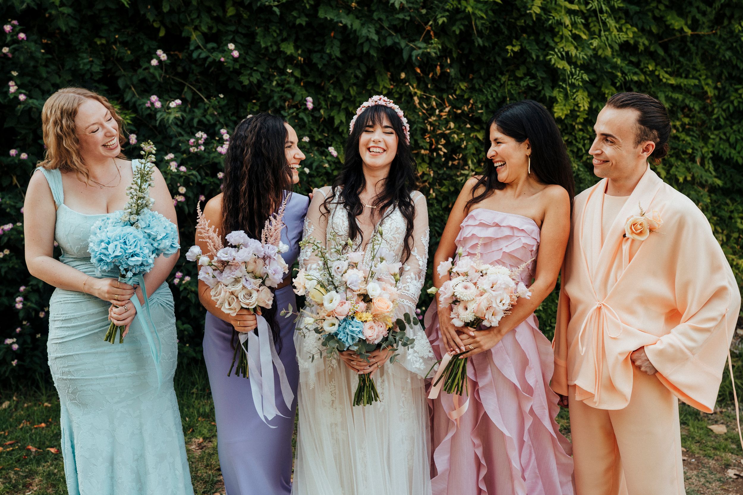 Bridesmaids in pastel dresses of mint, lavender, and blush pink hold bouquets while standing together outdoors.