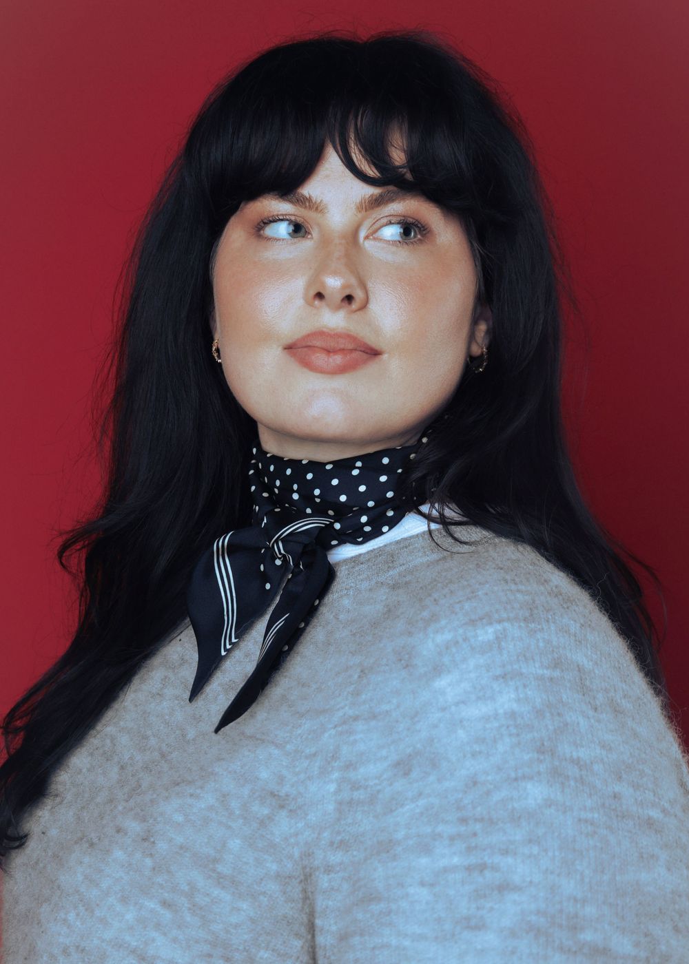 A portrait series against a red background shows someone with dark bangs in a polka dot collar and gray sweater.