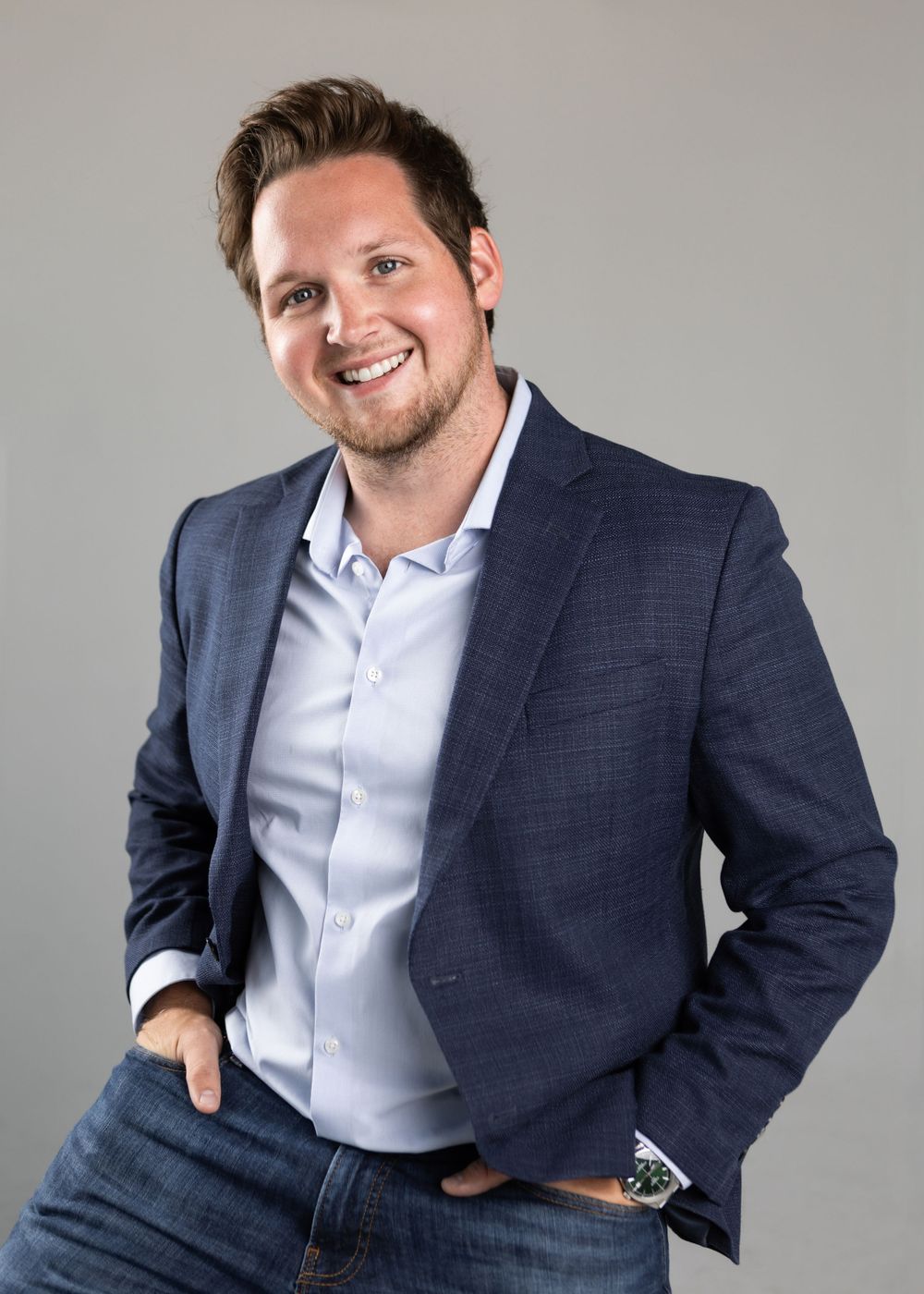 Professional headshot of person in navy blazer and light blue shirt against grey background.