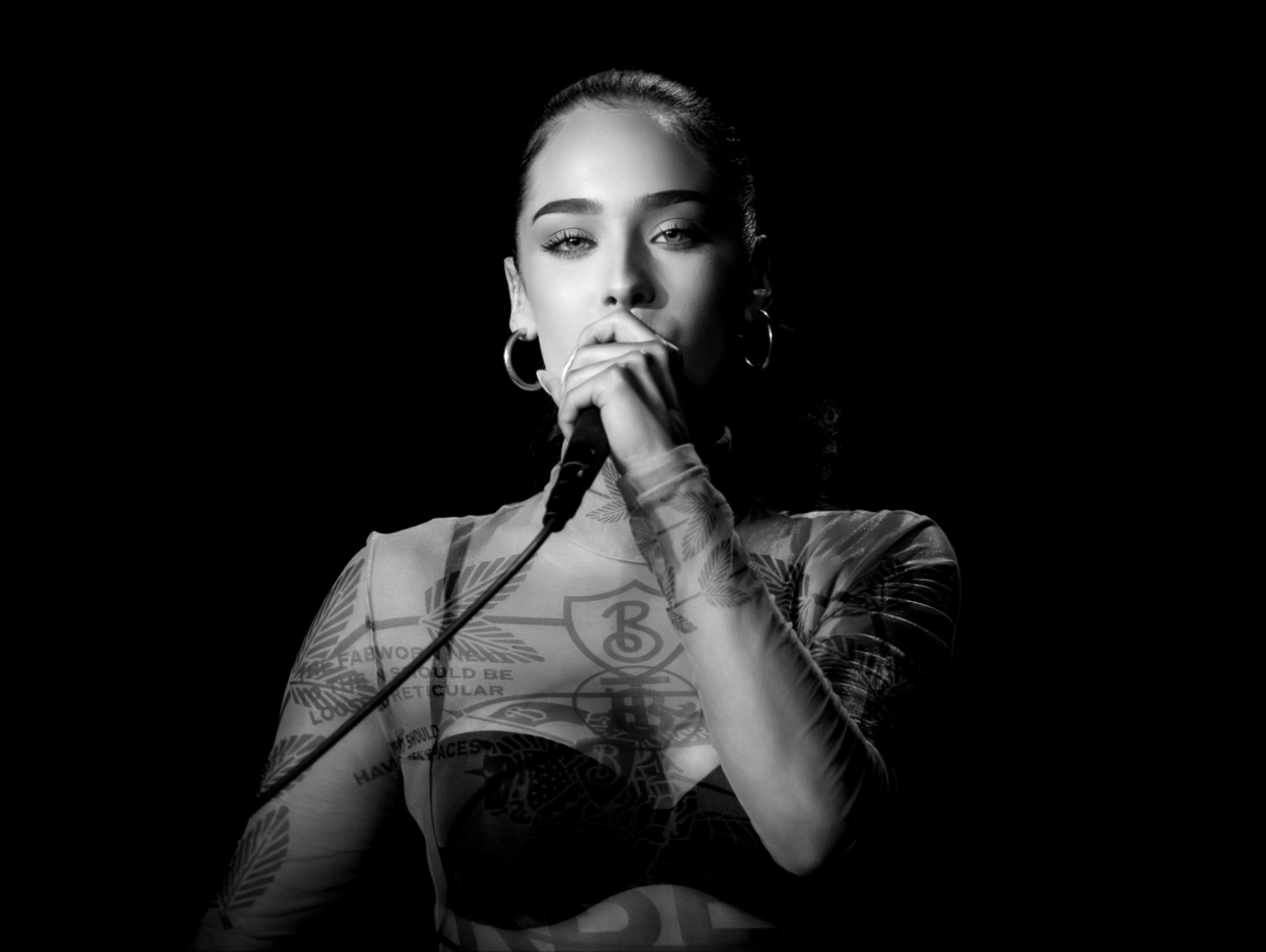 Black and white photo of performer singing into microphone on dark stage.