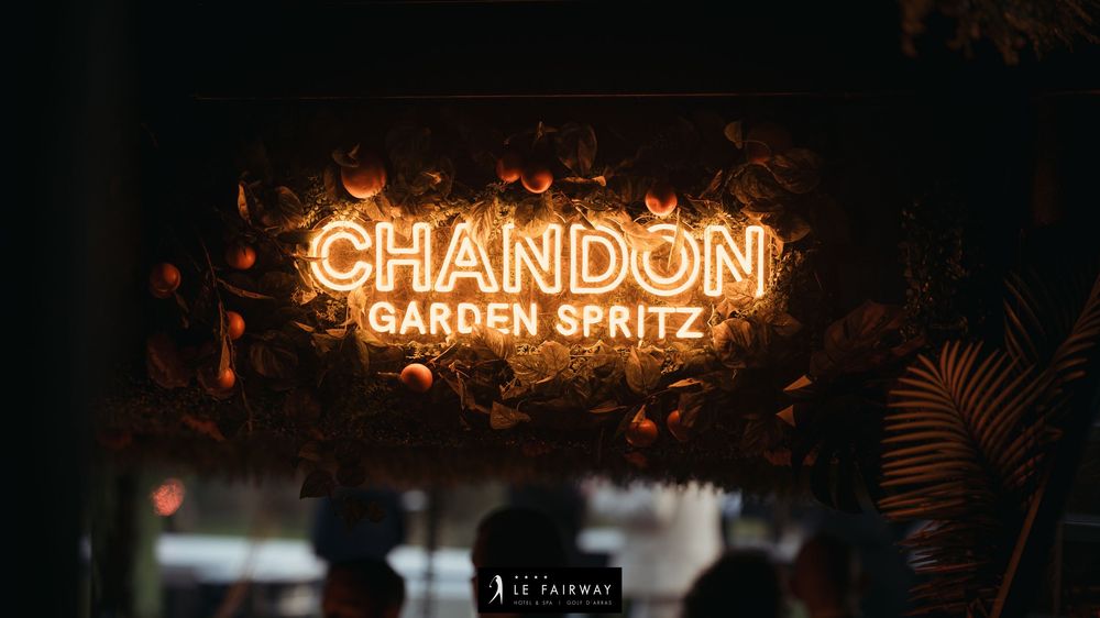 Glowing neon sign reading Chandon Garden Spritz surrounded by lush tropical foliage in dark setting.