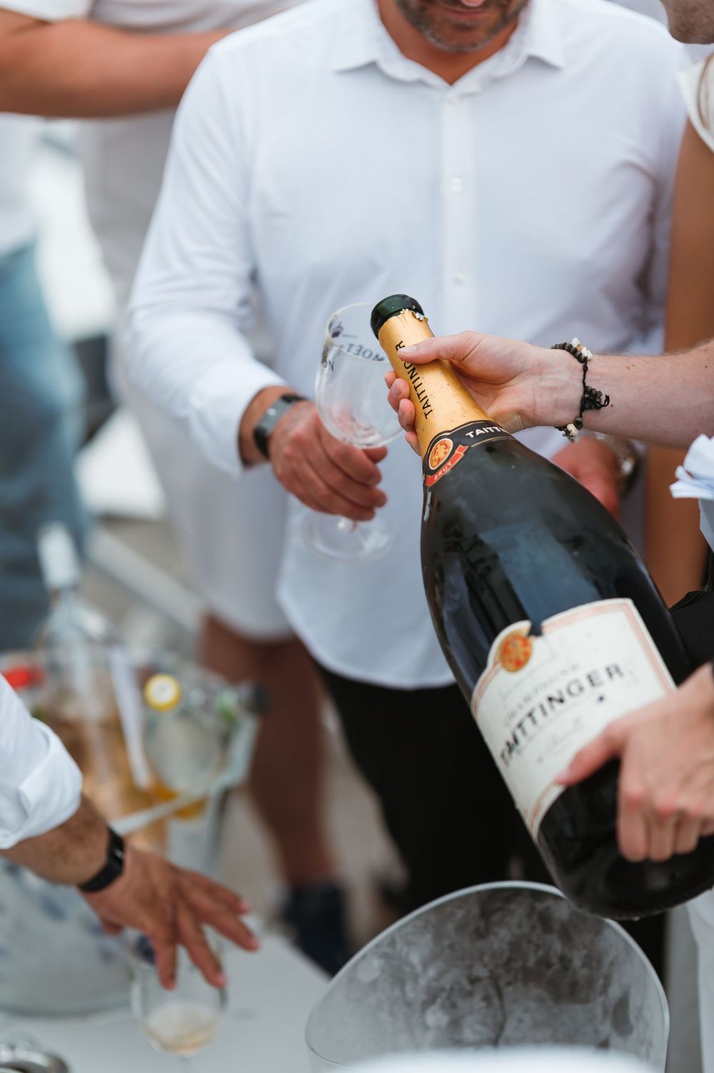 People pouring Taittinger champagne from a large bottle into glasses at an outdoor event.