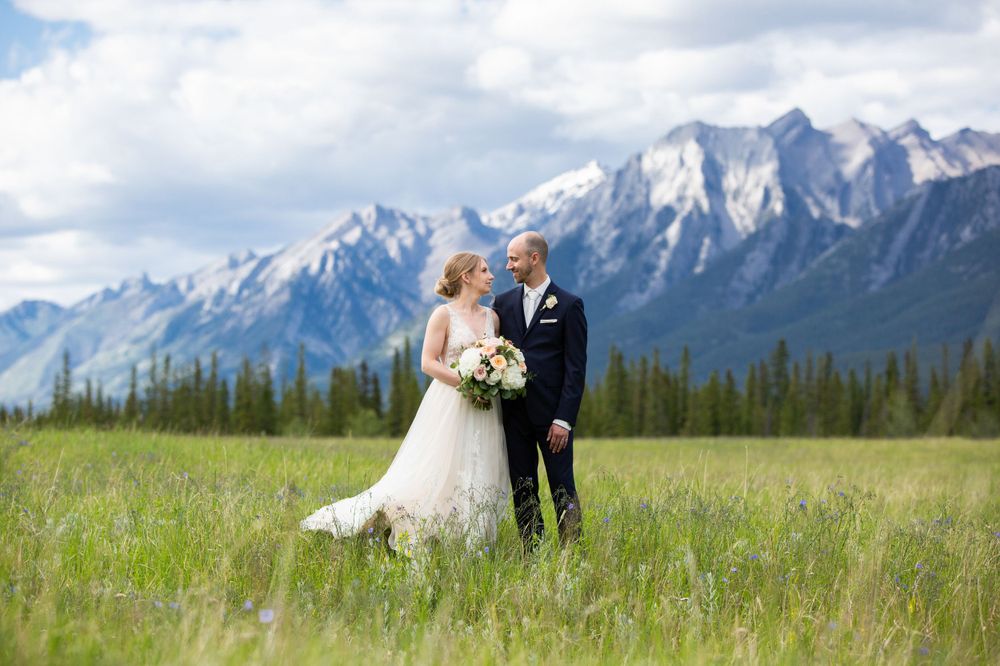 Bride and groom embracing in alpine meadow with stunning snow-capped mountain range behind them.