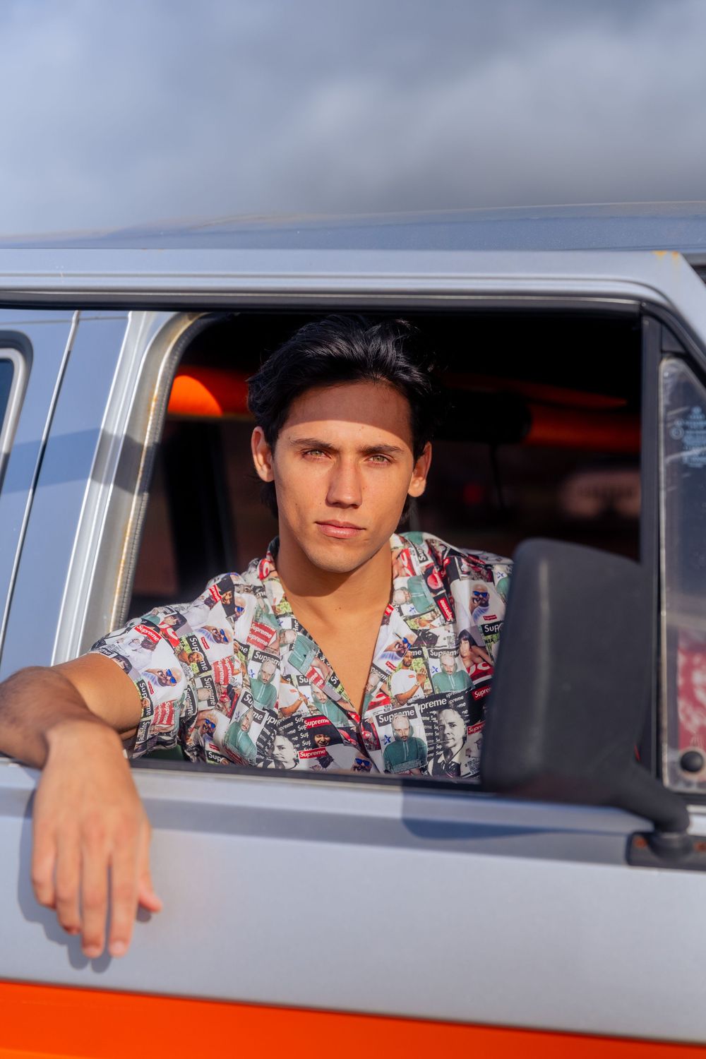 Young man in a printed shirt leaning out of a vintage van window with a confident gaze.
