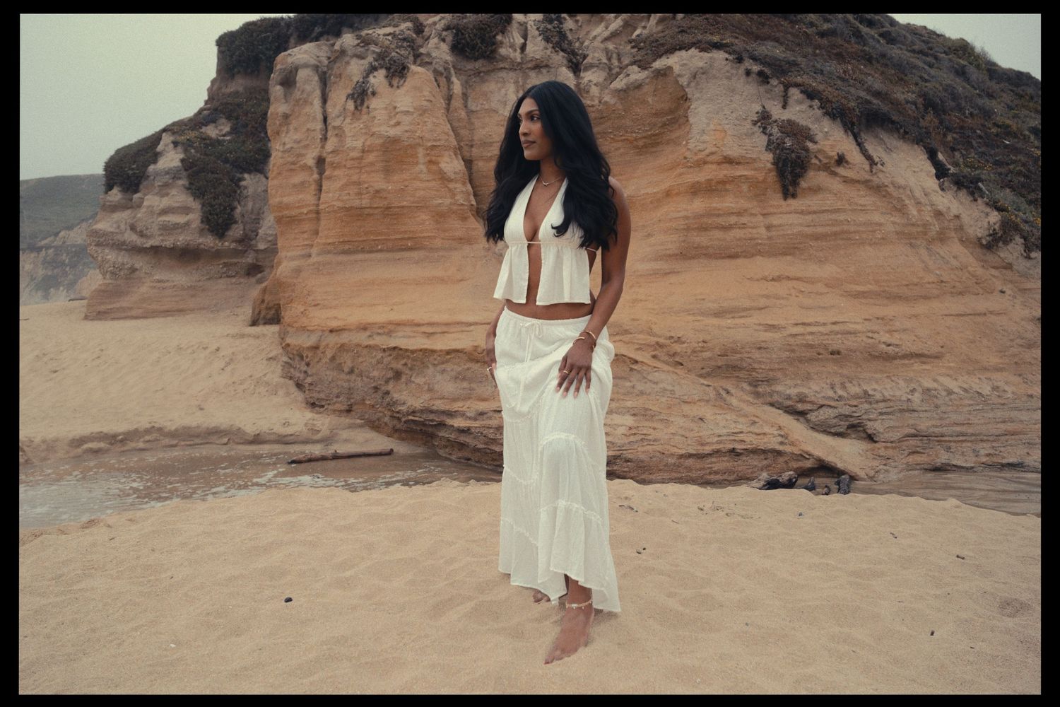 A person in a flowing white dress stands against dramatic red rock formations in a desert landscape.