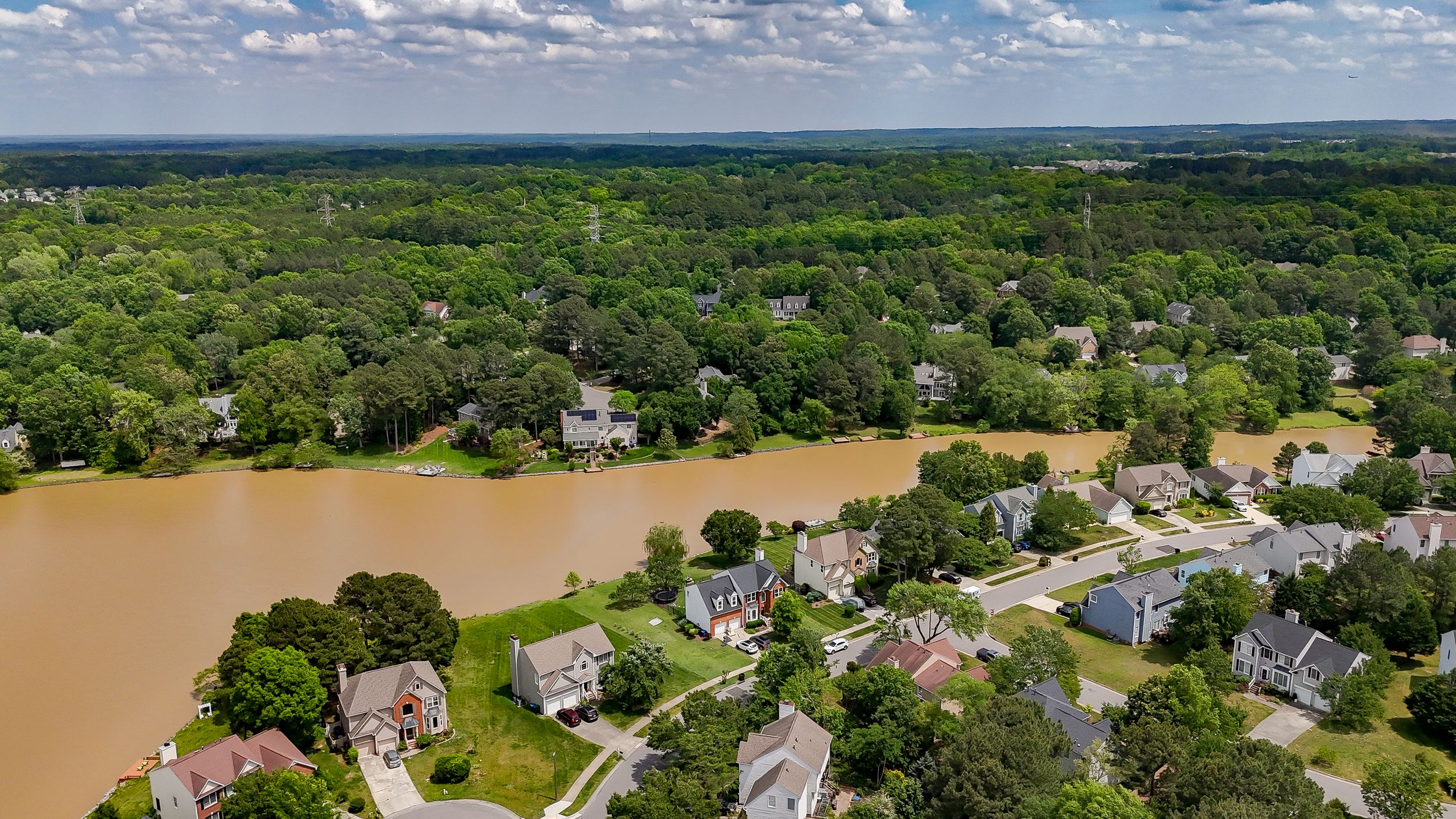 Panoramic aerial view of a lush green landscape with scattered buildings under a blue cloudy sky.
