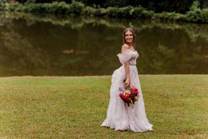 Bride in flowing dress holding vibrant red bouquet against natural outdoor backdrop.