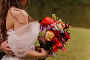 Wedding bouquet featuring bright red and colorful flowers in outdoor garden setting.