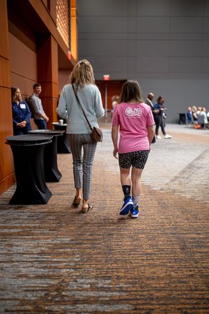 People's legs and feet walking on a patterned carpet in what appears to be a conference or event space.