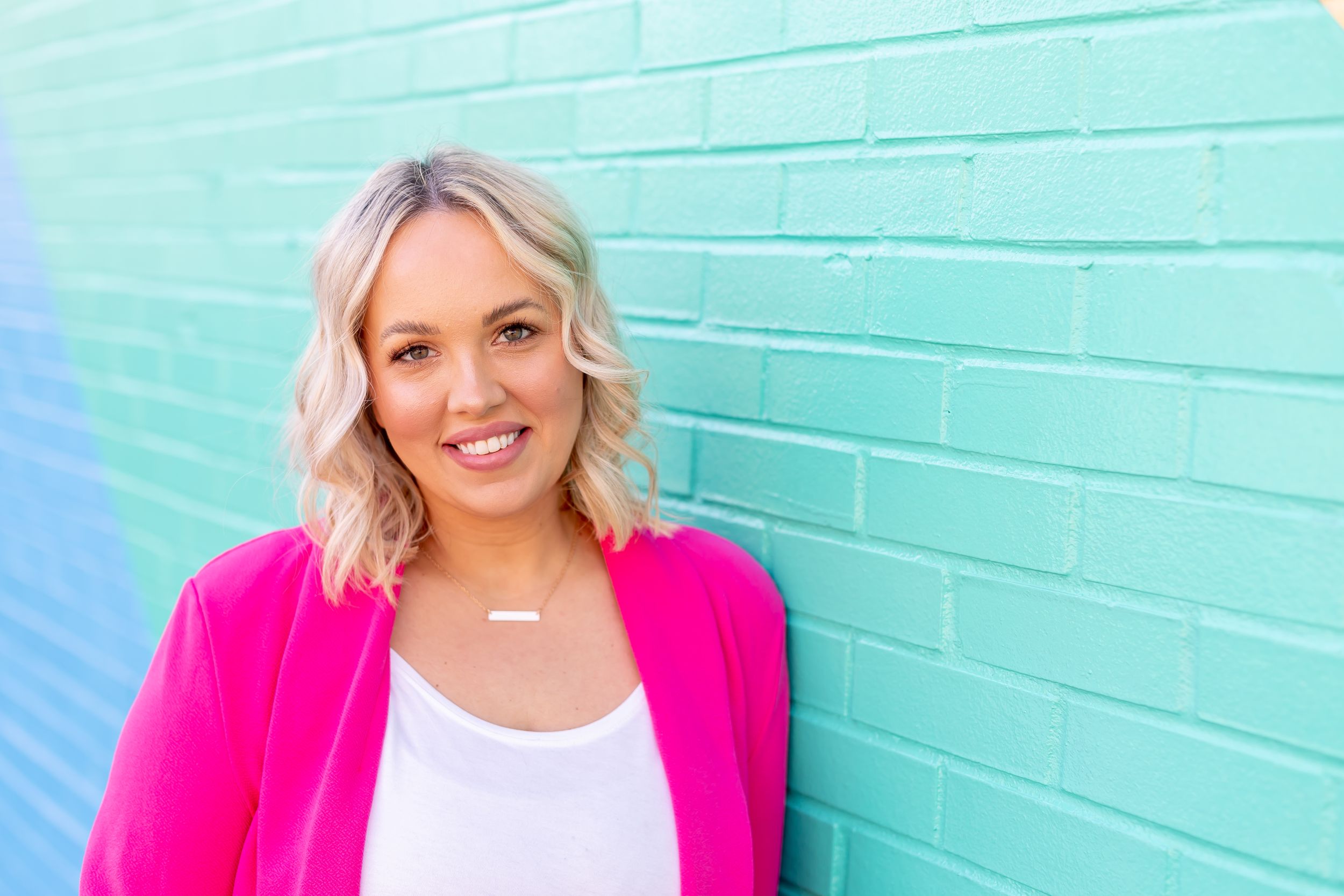 Professional headshot against turquoise wall featuring bright pink blazer and white top.