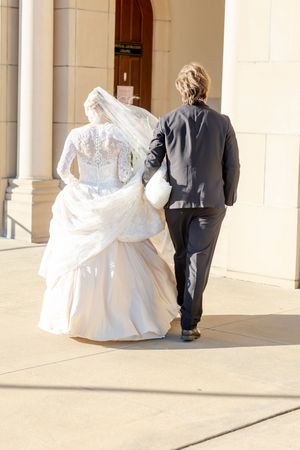 Couple walking along a columned walkway with flowing white wedding dress trailing behind.