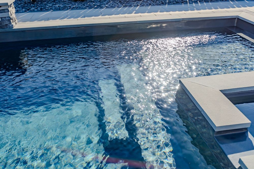 Swimming pool water surface with sunlight reflections creating dynamic blue patterns.