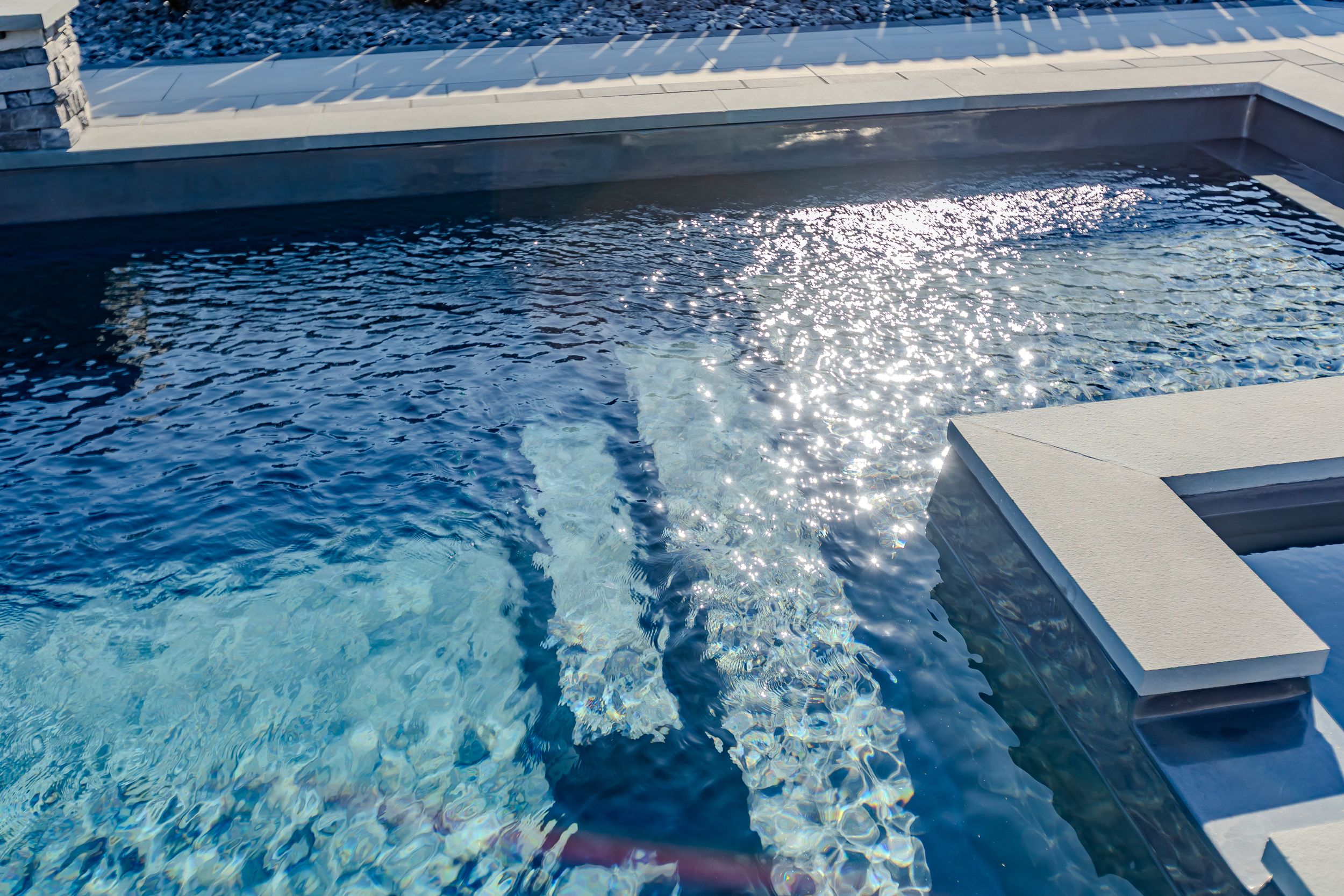 Swimming pool water surface with sunlight reflections creating dynamic blue patterns.