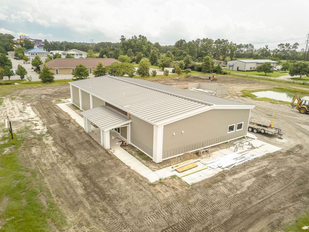 Aerial drone view of a large commercial building under construction with surrounding residential areas.