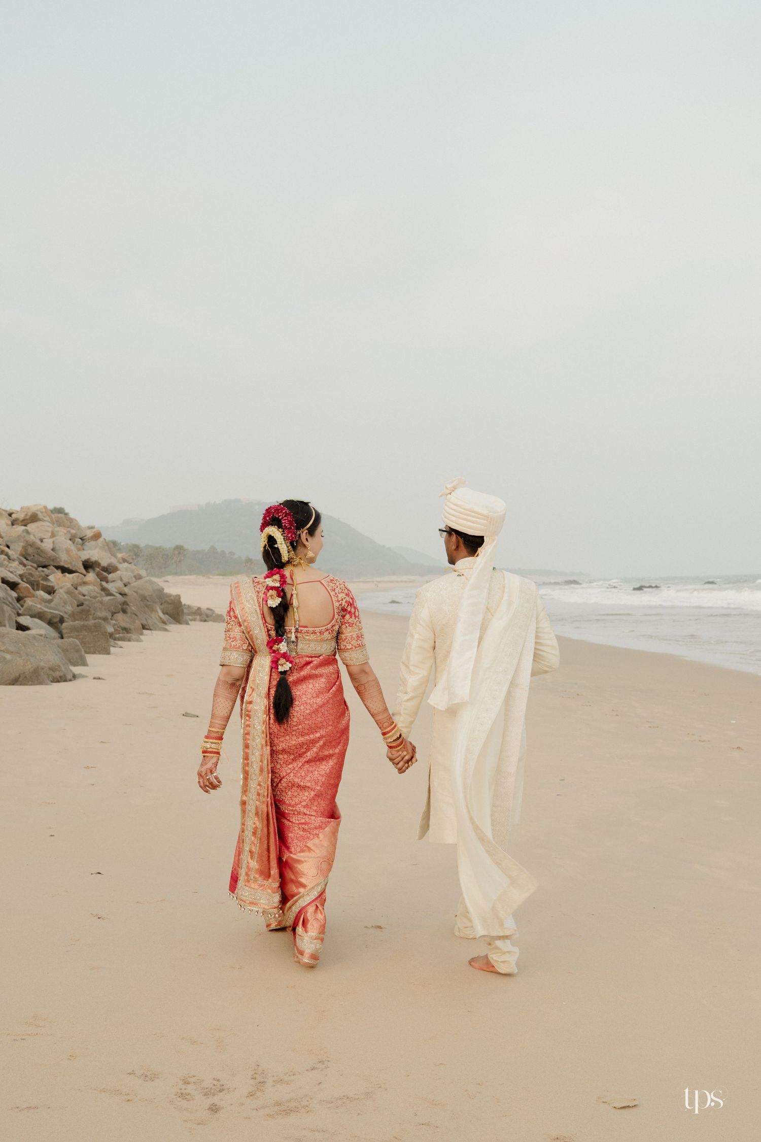 Indian bride and groom in traditional attire holding hands on a sandy beach romantic shot by a wedding photographer in Mumbai near me.