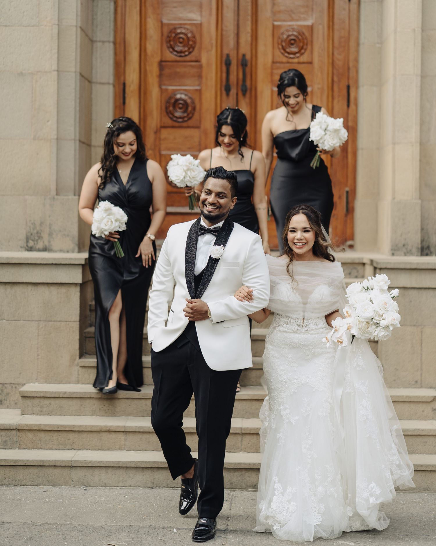 Wedding party celebrating on grand stone building steps with white floral bouquets, beautifully captured by a wedding photographer in Mumbai
