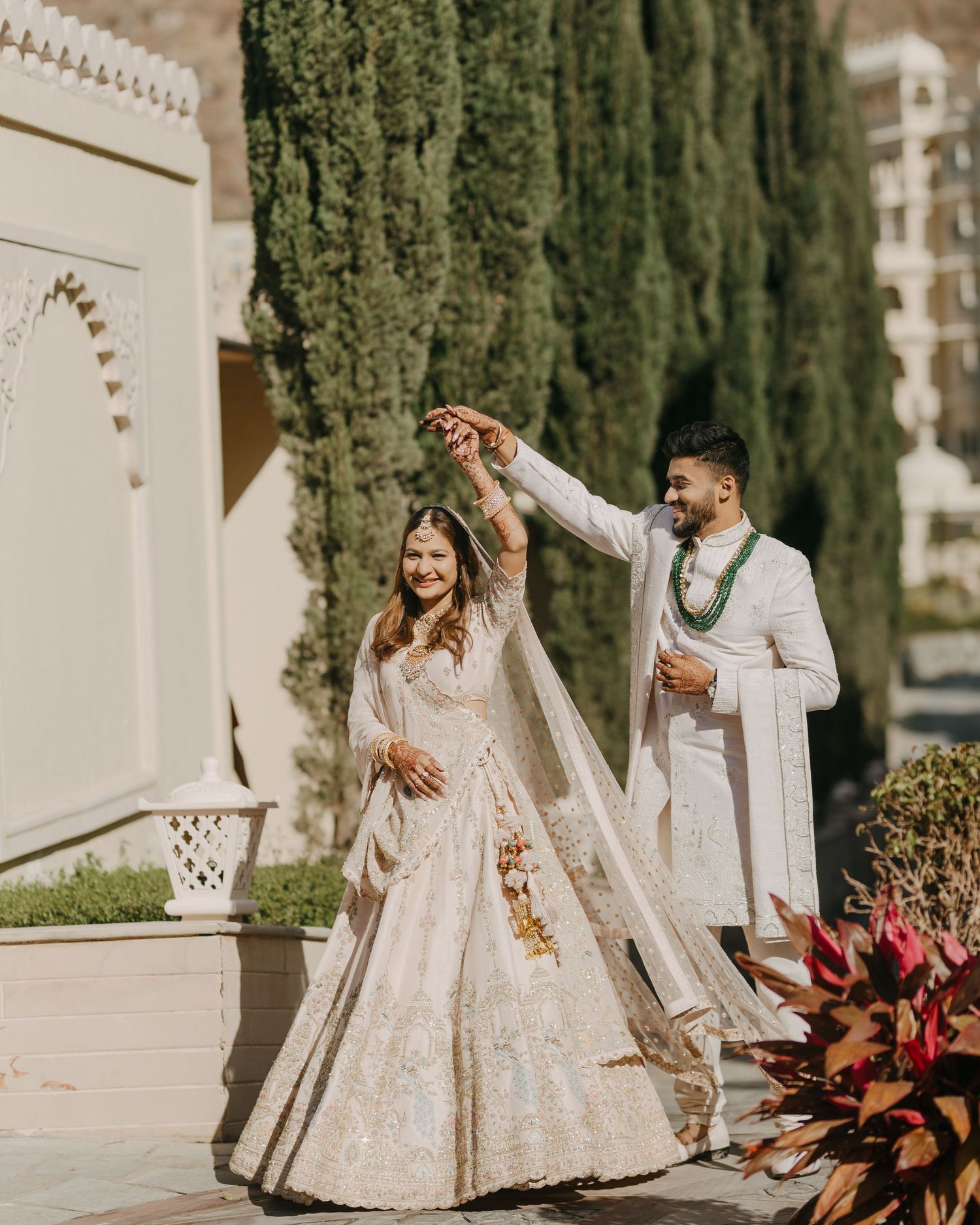 Stunning white & gold traditional wedding attire against cypress trees, elegantly shot by a trusted wedding photographer near me in Mumbai.