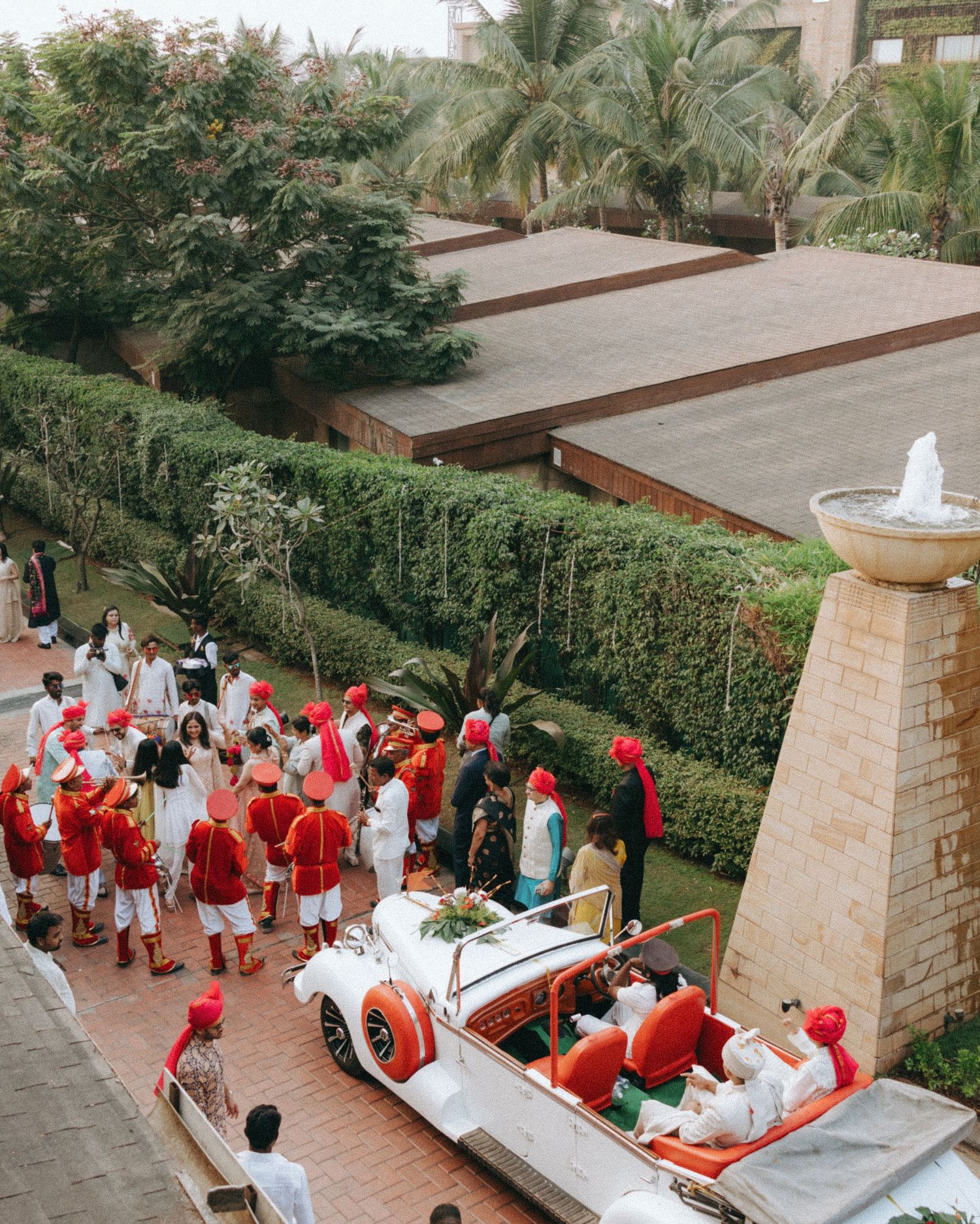 Group in red and white attire by a tropical fountain, captured by a wedding Photographer in Mumbai, the perfect Wedding photographer near me