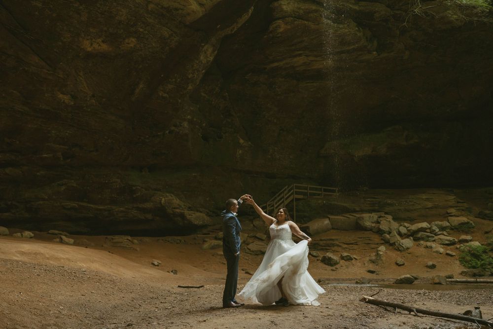 Groom spinning bride in white dress inside stunning sandstone cave, wedding dance in nature.