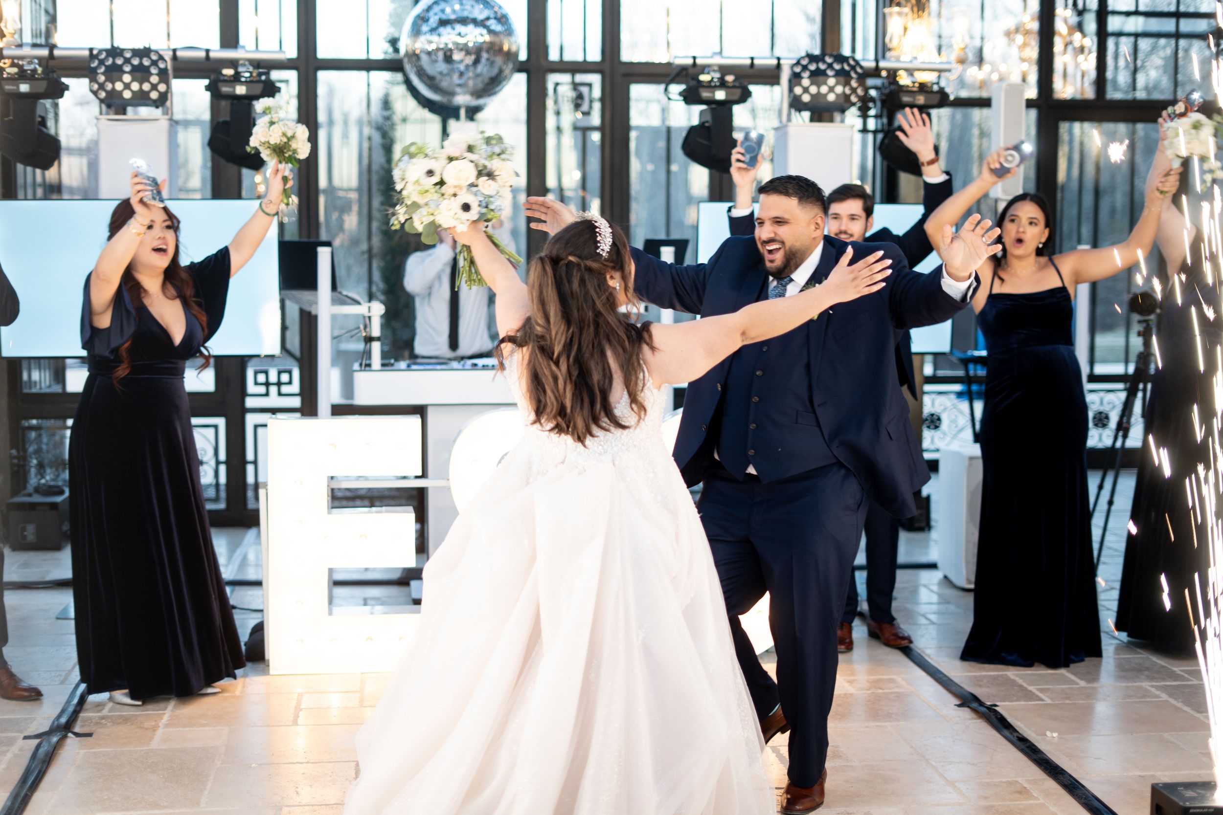 Wedding party celebrates during a reception with joyful dancing in an elegant venue with floor-to-ceiling windows.